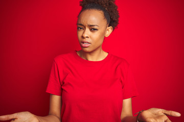 Sticker - Young beautiful african american woman with afro hair over isolated red background clueless and confused with open arms, no idea concept.