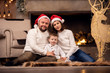 © Sergey Mironov - Photo of man and woman in Santa's cap with son sitting on floor on background of fireplace