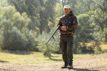 Wall Mural - Hunting period, autumn season open. A hunter with a gun in his hands in hunting clothes in the autumn forest in search of a trophy. A man stands with weapons and hunting dogs tracking down the game.	