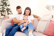 © gzorgz - Lovely family with their baby girl relaxing on sofa at home during Christmas
