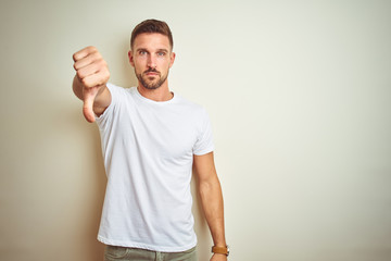 Sticker - Young handsome man wearing casual white t-shirt over isolated background looking unhappy and angry showing rejection and negative with thumbs down gesture. Bad expression.