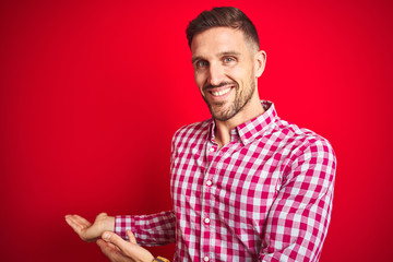 Young handsome man over red isolated background Inviting to enter smiling natural with open hand