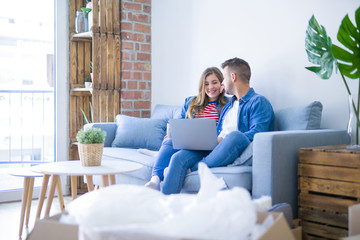 Poster - Young couple relaxing sitting on the sofa using the computer laptop around cardboard boxes, very happy moving to a new house