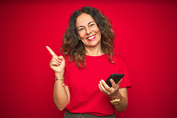 Wall Mural - middle age senior woman using smartphone over red isolated background very happy pointing with hand 