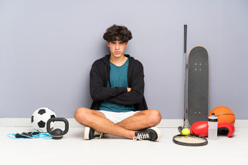 Young sport man sitting on the floor around many sport elements keeping arms crossed