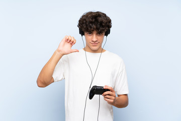 Young man playing with a video game controller over isolated blue wall proud and self-satisfied