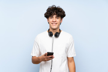 Young man listening music with a mobile over isolated blue wall smiling a lot