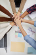© Seventyfour - Top view of multi-ethnic business team staking hands over meeting table in office, copy space