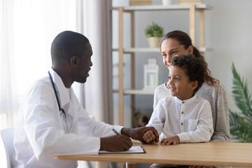 Wall Mural - Smiling mom with little son visiting african American doctor