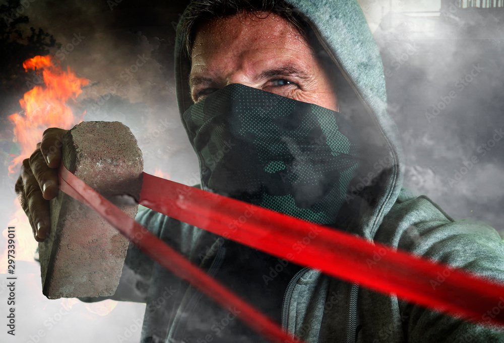 young man as ultra and radical anarchist rioter . furious antifa protester in face mask throwing brick hostile on street on demonstration in violet riot and chaos - obrazy, fototapety, plakaty 