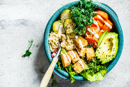 buddha bowl with quinoa, tofu, avocado, sweet potato, brussels sprouts and tahini dressing, top view