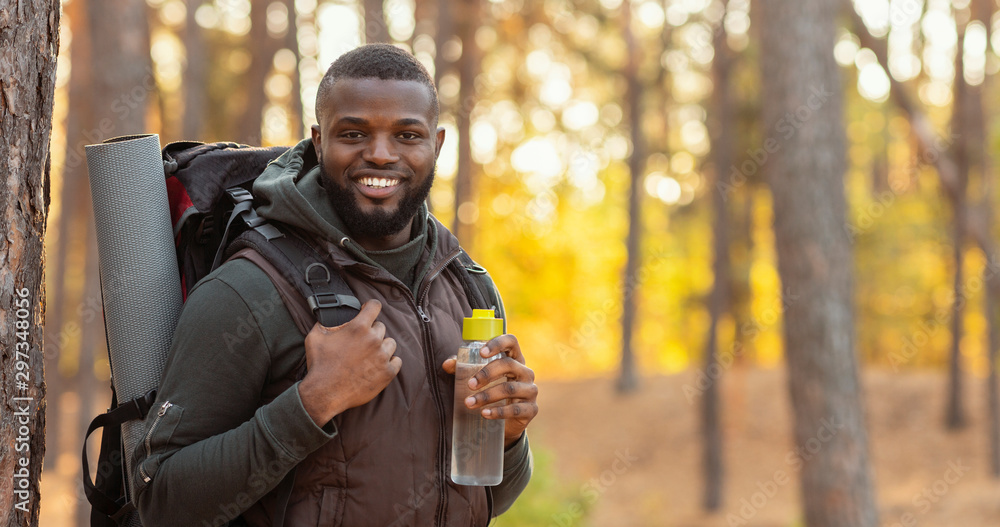 Happy guy with backpack smiling over forest background - obrazy, fototapety, plakaty 
