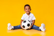 © Prostock-studio - Portrait of cute little boy with soccer ball sitting over yellow studio background