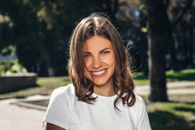 Portrait Of A Young Cute Girl In A White T-shirt With A Smile In The Park. Attractive Girl Smiling In The Park And Looking At The Camera