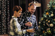 © spaskov - Young married couple at home in casual clothes, a man and a woman decorate the Christmas tree.