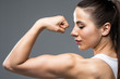Portrait of a beautiful fitness woman showing her biceps isolated on gray background