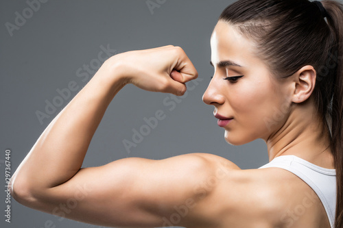 Fotomural Portrait of a beautiful fitness woman showing her biceps isolated on gray backgr