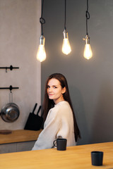 Portrait of a young beautiful woman in a warm sweater and with a cup of hot drink at home on the background of a window. Lamps of warm light.