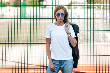 Wall Mural - Girl wearing t-shirt, glasses and leather jacket posing against street , urban clothing style. Street photography