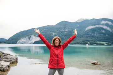 Sticker - A senior woman hiker standing by lake in nature, stretching arms.