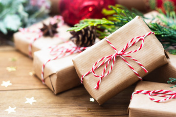 Close up Christmas gift boxes wraped in craft paper, fir branches, red baubles, pine cones over wooden table prepared for celebrating festive holiday season.