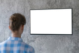 Fototapeta Nowy Jork - Mockup image - woman watching flat smart led TV with white blank screen hanging on wall in the living room at home. Mock up, copyspace, leisure time, template, entertainment and technology concept