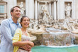 Rome travel tourists couple at Trevi Fountain in Rome, Italy vacation. Happy young romantic interracial couple traveling in Europe. Man and Asian woman embracing together.