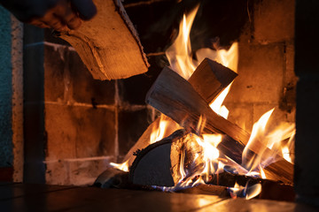 Hands put firewood in a kindled fireplace on a cold winter day. Warmth and comfort in the house.