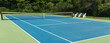 Sie view of blue tennis court with green boarder and benches to rest on