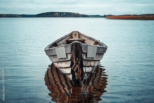 Cuadros en Lienzo Wooden rowing boat with reflection in a still lake water at dusk.