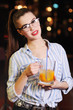 © Evgeniy Kalinovskiy - a beautiful young girl with glasses is holding a mug with beer or a beer orange cocktail in front of a bar or a pub