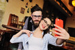 © Evgeniy Kalinovskiy - young couple - guy and girl posing and grimacing on the smartphone's camera, making selfie on the background of the bar.