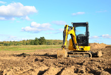 Mini Excavator Digging Earth In A Field Or Forest. Laying Underground Sewer Pipes During The Construction Of A House. Digging Trenches For A Gas Pipeline Or Oil Pipeline. Earthwork, Foundation Pit