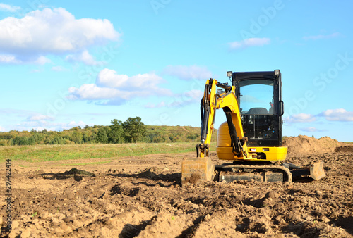 Mini excavator digging earth in a field or forest. Laying underground sewer pipes during the construction of a house. Digging trenches for a gas pipeline or oil pipeline. Earthwork, foundation pit