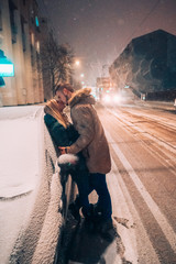 Young adult couple kissing each other on snow covered street