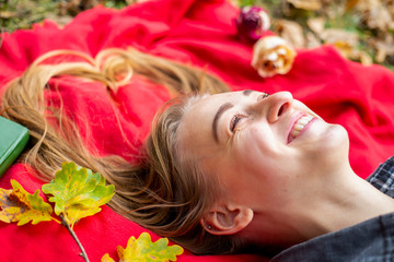 Teenager. Young beautiful white teenage girl in casual clothes lies on a red plaid on the street in the park in the autumn evening.