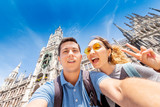 Fototapeta Paryż - happy multinational couple in love hugs and takes a selfie photo on the background of The city hall tower in Munich. Honeymoon trip to Germany