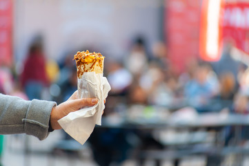 female's hand in grey coat holding toner kebab or burrito on blurred festival background