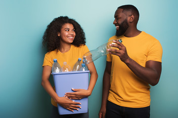 Wall Mural - Happy couple hold a plastic container with bottles over a light blue color. Concept of ecology, conservation, recycling and sustainability