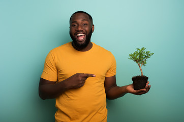 Wall Mural - Happy boy indicates a small tree ready to be planted over a light blue color. Concept of forestation, ecology and conservation