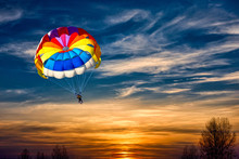 A Man Is Gliding With A Parachute On The Background Of Sunset.