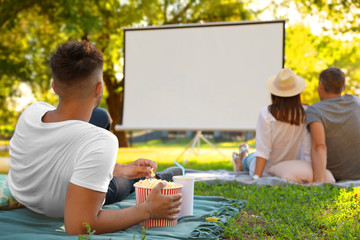 Wall Mural - Young man with popcorn watching movie in open air cinema. Space for text