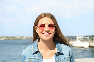 Poster - Young woman wearing stylish sunglasses near river