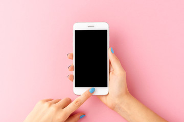 overhead shot of woman’s hands holding mobile phone with empty screen on pink background. top view