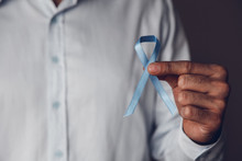 Man Doctor's Hands Holding A Blue Ribbon In Front Of Him. Prostate Cancer Awareness Month. Men's Cancer Concept