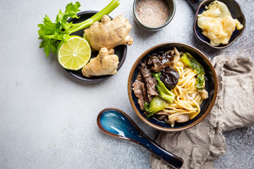 Wall Mural - Asian ramen noodles soup with beef, oyster mushrooms and vegetables in bowl on gray background, top view