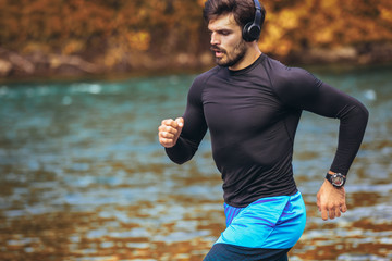 Handsome young man jogging on river bank