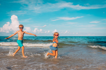 Wall Mural - happy little girl and boy run fly play with waves on beach