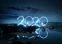 Night Time 2020 Light Effect Writing Reflecting In Water On A Beach. Long Exposure Landscape New Year Photo Composite.