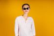 © mnelen.com - fashionable stylish girl with glasses, raised eyebrows questioningly, her hair gathered in a bun, dressed in a white shirt. studio yellow
